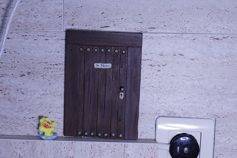Pequeña puerta de madera del Ratoncito Pérez en la pared de la clínica, junto a un juguete