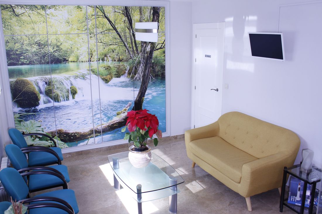 Sala de espera de la Clínica Dental Javier Corzo en Granada, con sofá amarillo y sillas azules